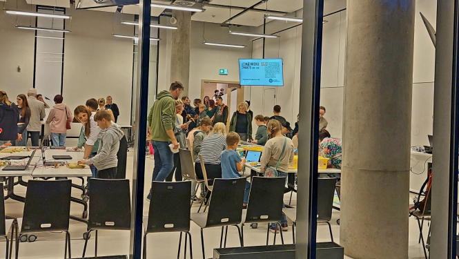 Caur logu redzami Zinātnieku nakts dalībnieki universitātes telpās. 