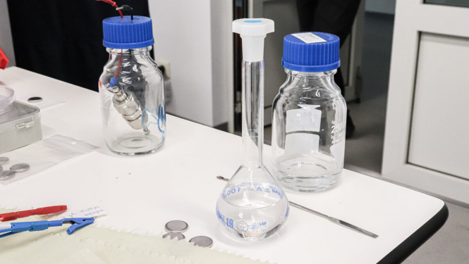 Laboratorijas galds, tukša kolba un pudelītes ar ziliem korķiem. 