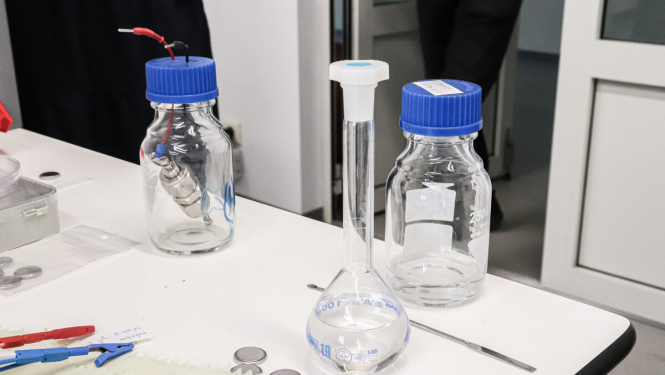 Laboratorijas galds, tukša kolba un pudelītes ar ziliem korķiem. 