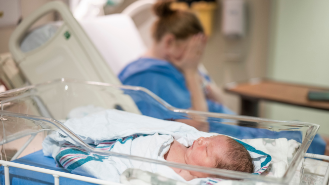 Mazulis slimnīcas gultiņā ar mammu fonā